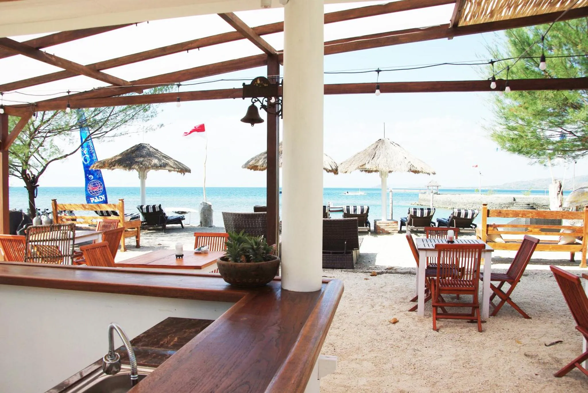 Un bar en bois s'ouvre sur une terrasse avec tables et chaises face à la mer.