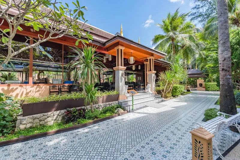 Terrasse ombragée avec tables et chaises devant un bâtiment tropical.