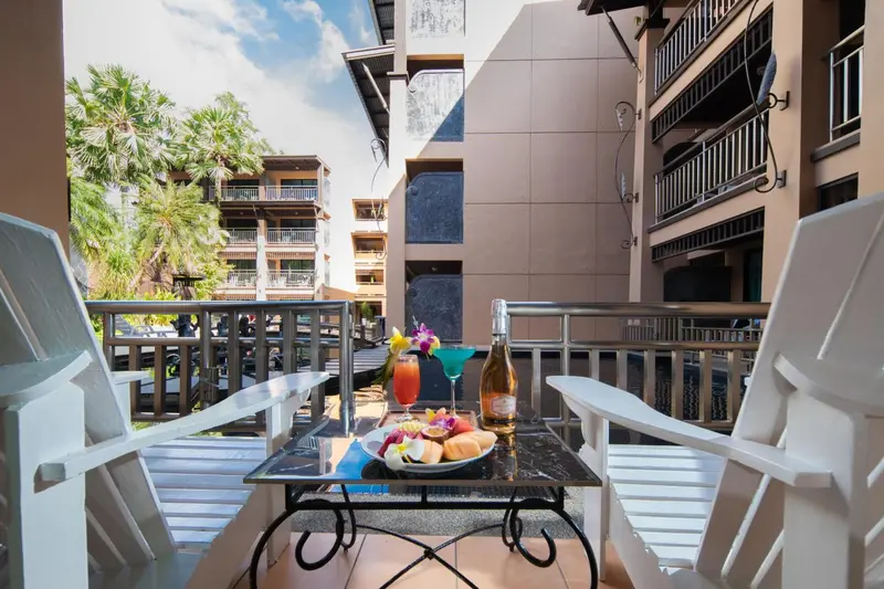 Deux fauteuils blancs sur un balcon avec une table garnie de boissons et de fruits.