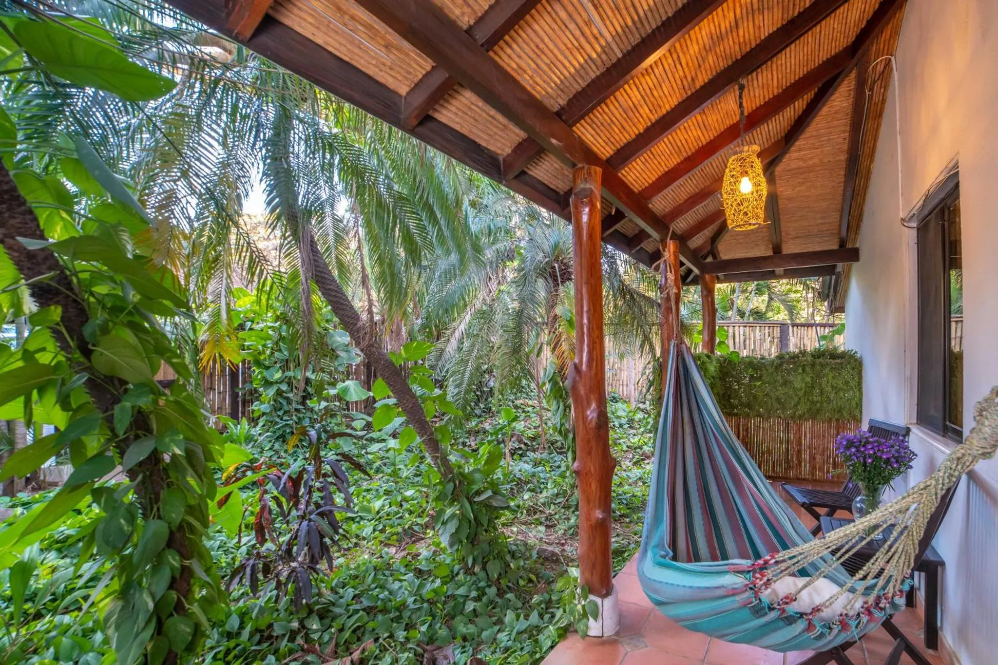Un hamac coloré est suspendu sur une terrasse ombragée par une végétation luxuriante.
