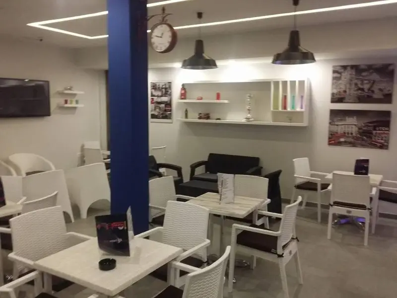 Une salle lumineuse avec des tables et des chaises blanches, des suspensions noires et des décorations murales.