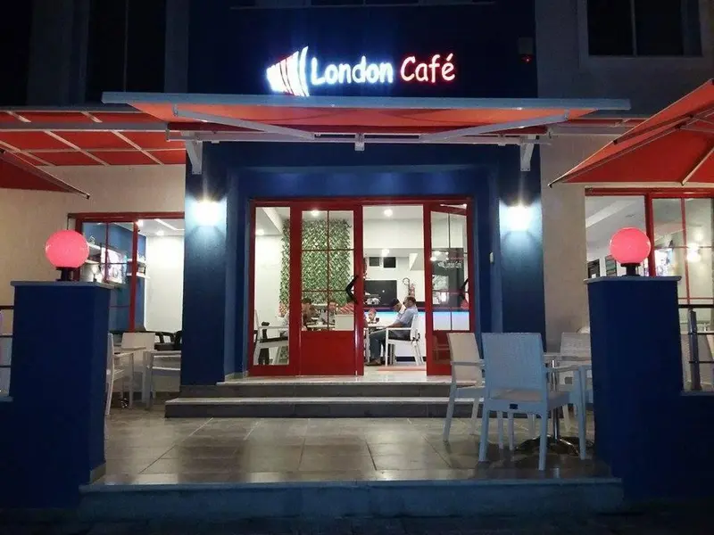 Façade d'un café avec une marquise rouge et des tables en terrasse.