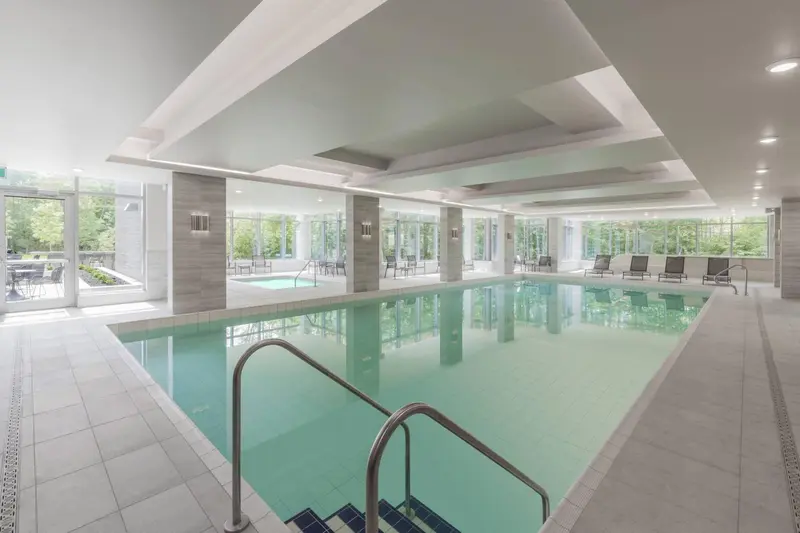 Une piscine intérieure rectangulaire avec des baignoires à remous et des fenêtres donnant sur un jardin.