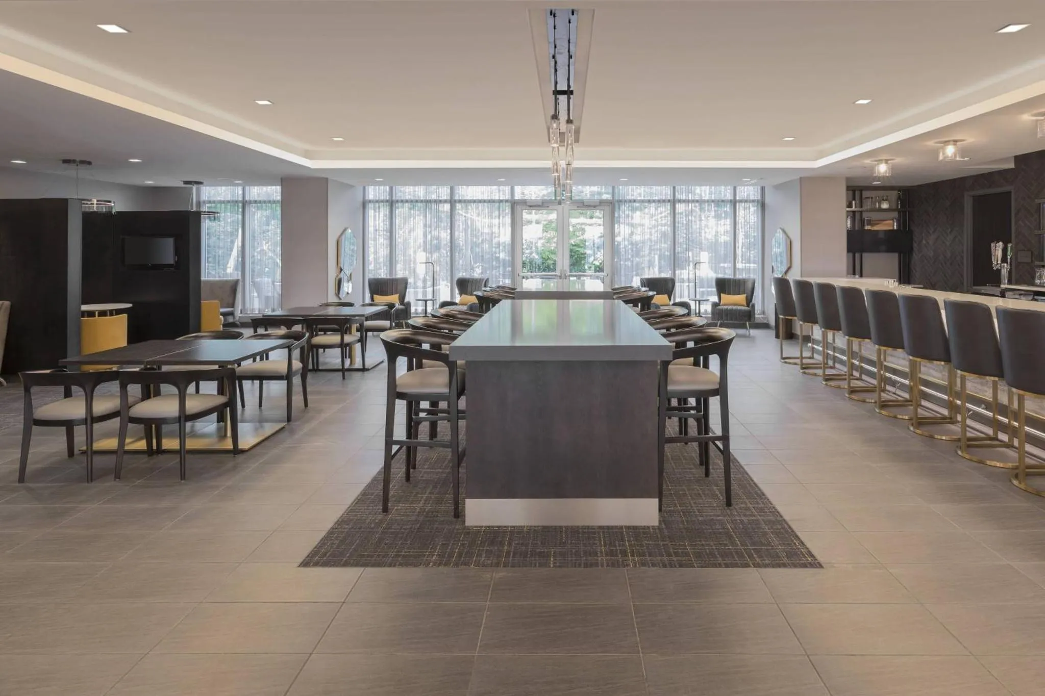 Une grande salle lumineuse avec des tables et des chaises, ainsi qu'un long comptoir avec des tabourets.