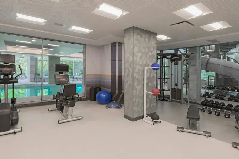 Une salle de sport lumineuse avec des équipements de musculation et une vue sur une piscine extérieure.