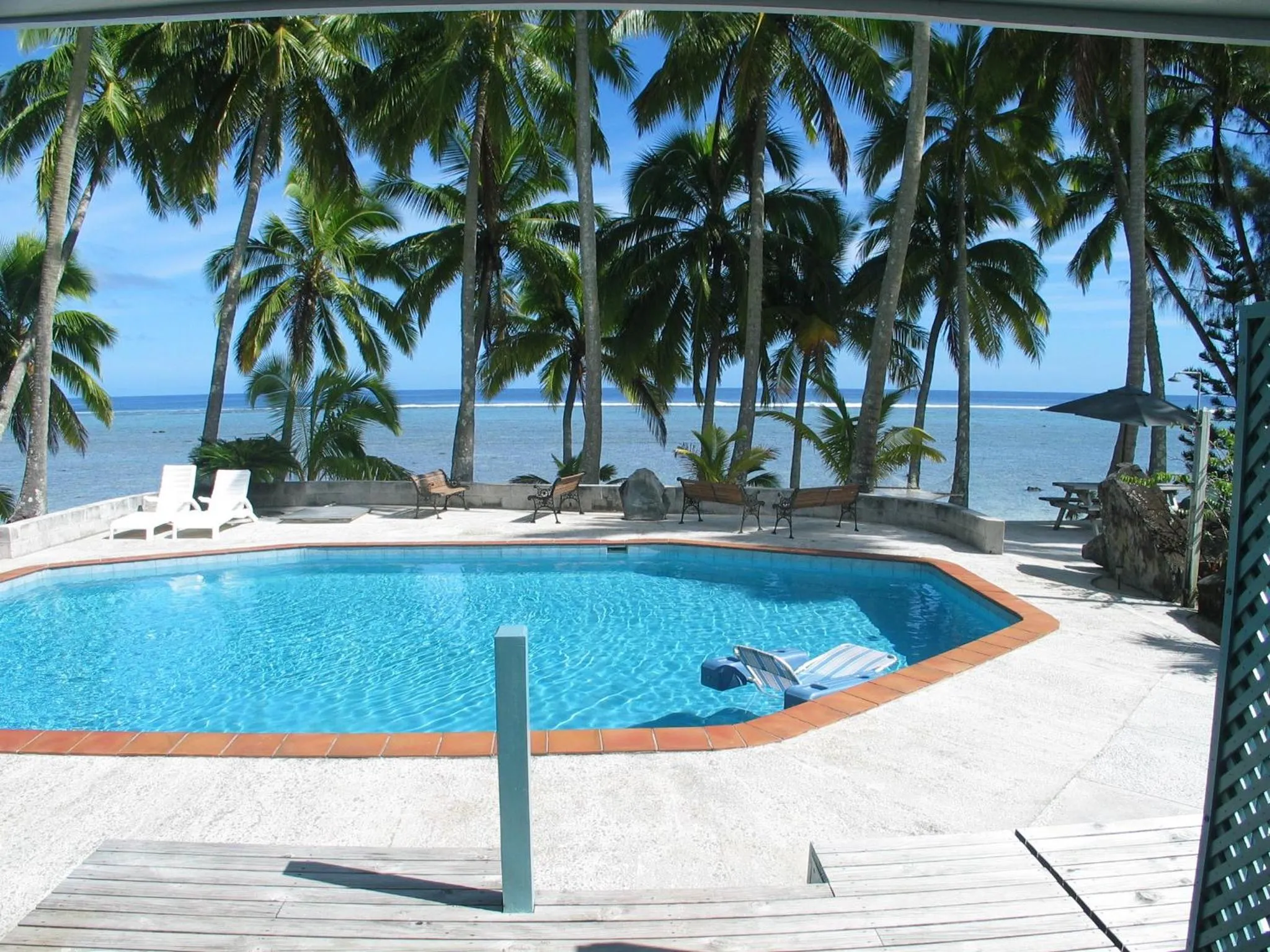 Une piscine turquoise bordée de chaises longues offre une vue sur la mer et les palmiers.