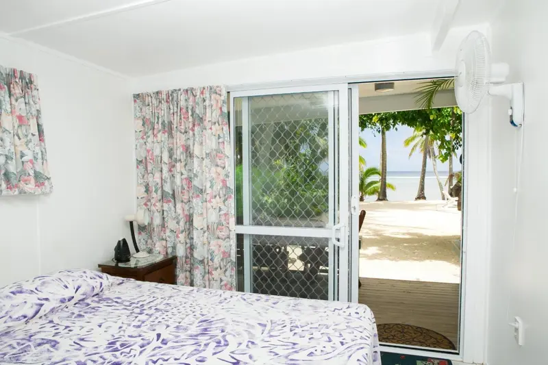 Une chambre lumineuse s'ouvre sur une vue de plage et de végétation tropicale.