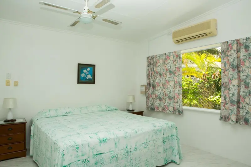 Une chambre lumineuse avec un lit recouvert d'une courtepointe verte et des rideaux fleuris.
