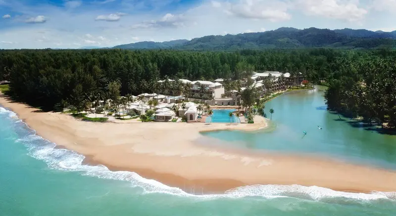 Vue aérienne d'un complexe hôtelier bordant une plage de sable fin et une mangrove.