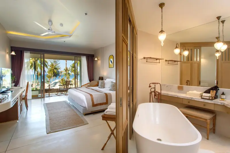 Une chambre lumineuse avec un lit king-size et une salle de bain attenante donnant sur une vue tropicale.