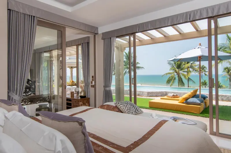Une chambre avec un grand lit donnant sur une piscine et la mer.