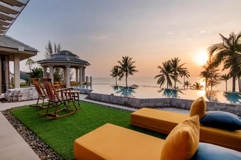 Transats et mobilier de jardin face à une piscine à débordement avec vue sur la mer au coucher du soleil.