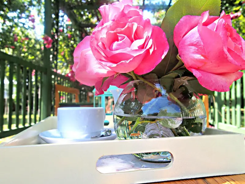 Un plateau blanc présente une tasse de café et un bouquet de roses roses.