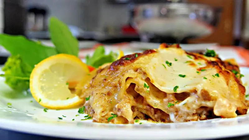 Une portion de lasagnes gratinées est présentée sur une assiette blanche, accompagnée d'une tranche de citron et de quelques feuilles de salade.