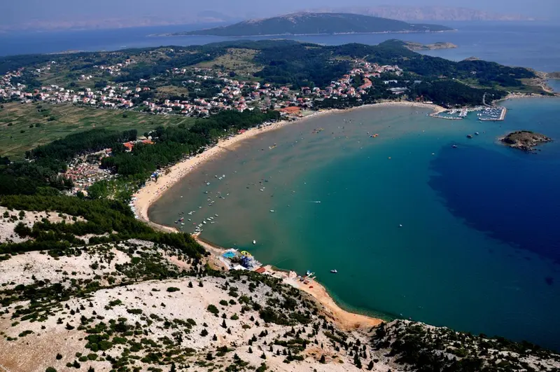 Vue aérienne d'une plage de sable fin bordée d'une eau turquoise et d'une végétation verdoyante.