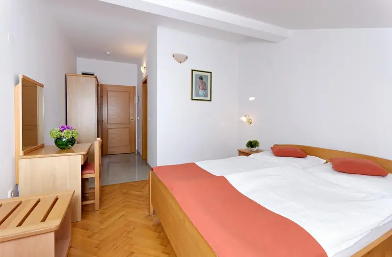 Une chambre lumineuse avec un lit recouvert d'une couverture orange et un bureau en bois.