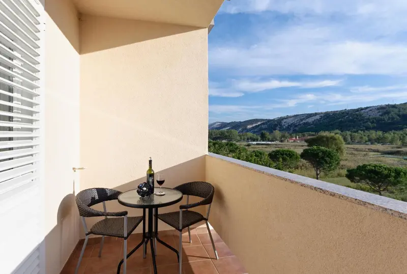 Une petite table ronde avec deux chaises sur un balcon ensoleillé offre une vue sur un paysage montagneux.