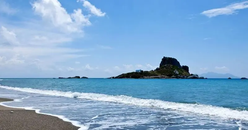 Une plage de sable fin borde une mer turquoise sous un ciel bleu.