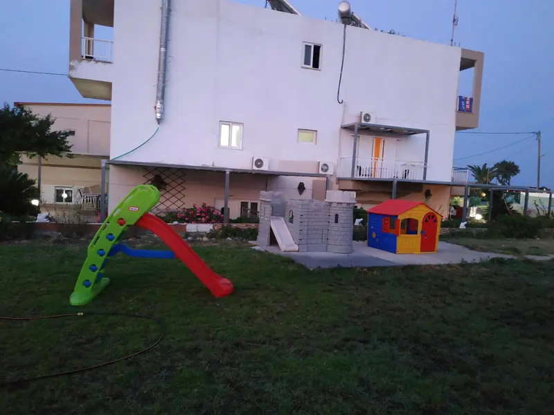 Bâtiment blanc avec des aires de jeux pour enfants dans un jardin verdoyant.