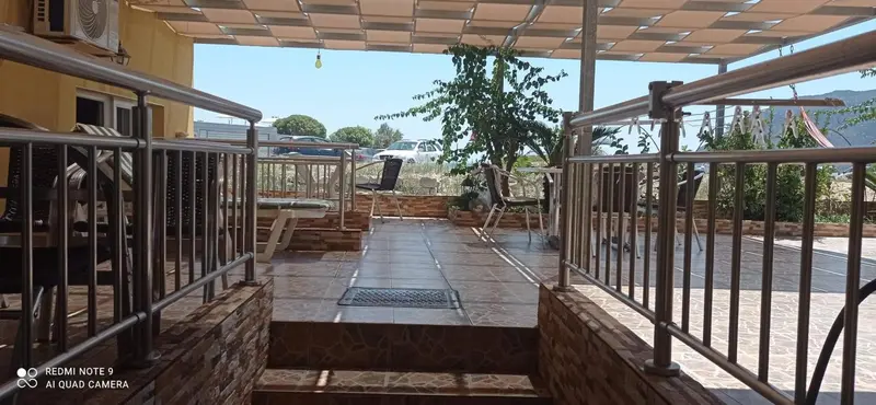 Terrasse ombragée avec mobilier de jardin et vue sur un paysage montagneux.