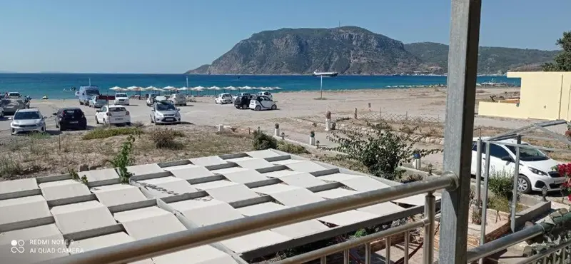 Vue sur une plage ensoleillée avec des transats et des véhicules garés.