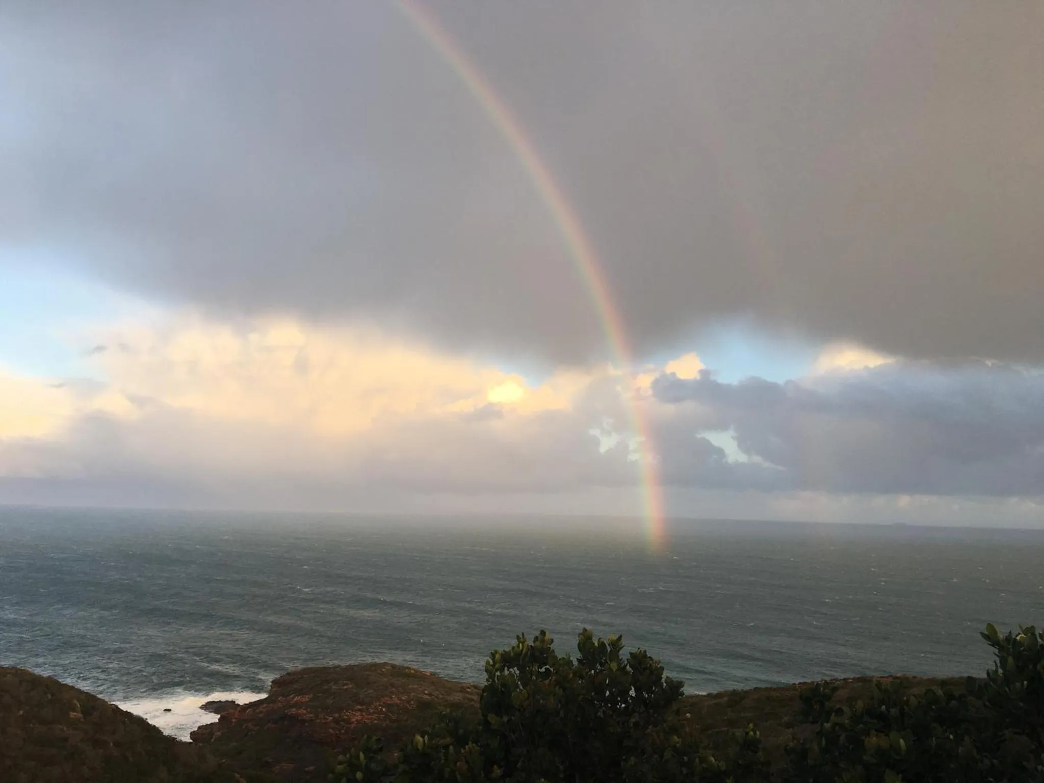 Un arc-en-ciel se dessine au-dessus de l'océan sous un ciel nuageux.