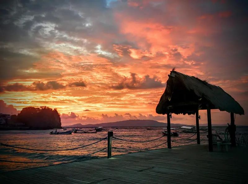 Un abri de plage en chaume se dresse face à un coucher de soleil flamboyant sur l'océan.