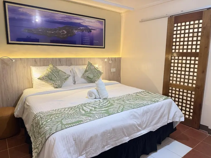 Une chambre lumineuse avec un grand lit recouvert d'une couette blanche et de coussins verts.