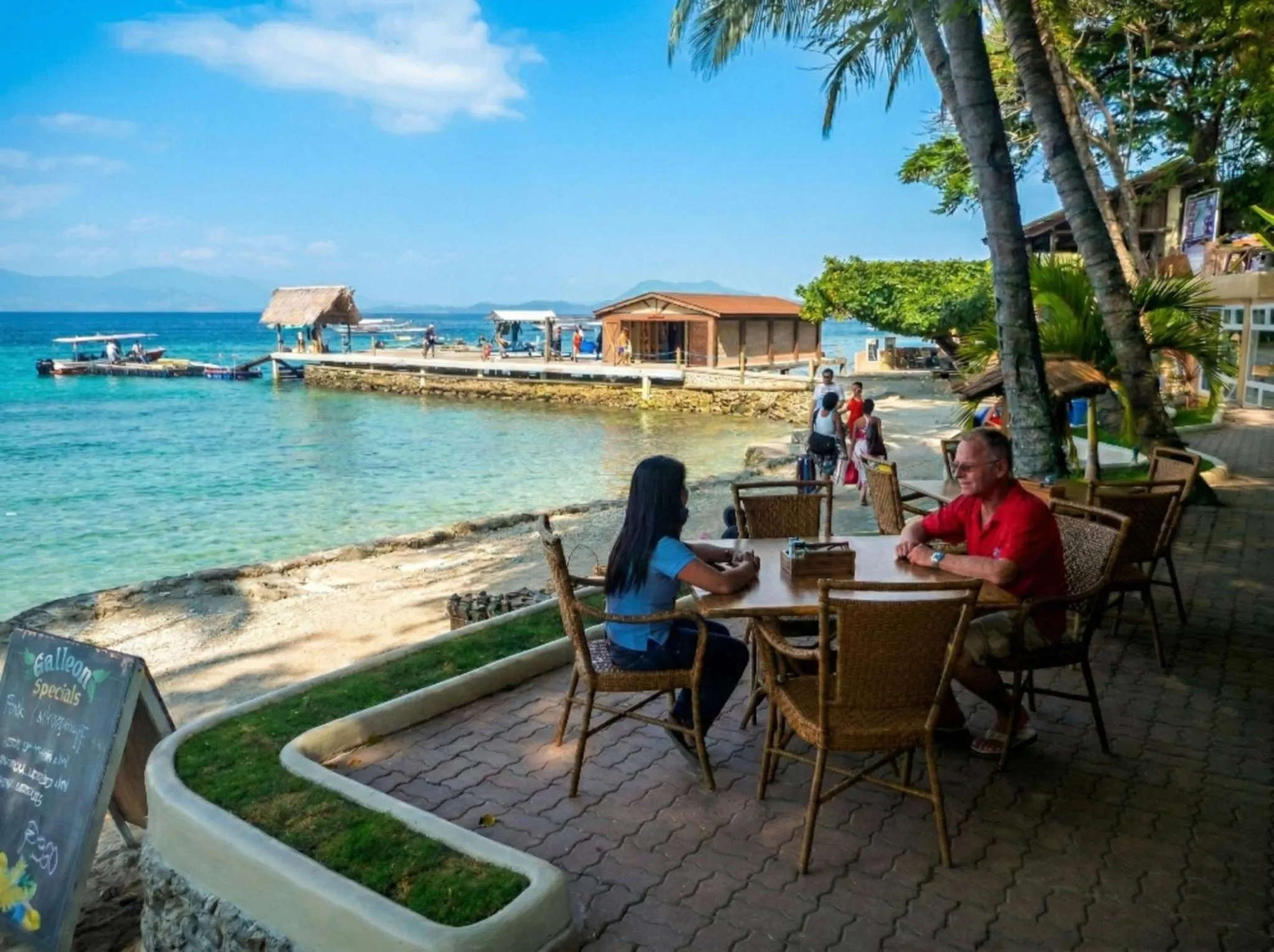 Deux personnes sont assises à une table sur une terrasse en bord de mer.