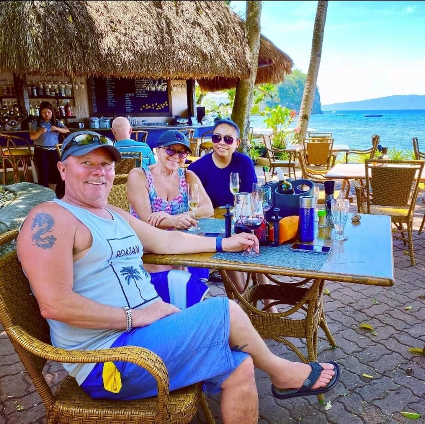 Des clients sont assis à une table en osier sur une terrasse en bord de mer.
