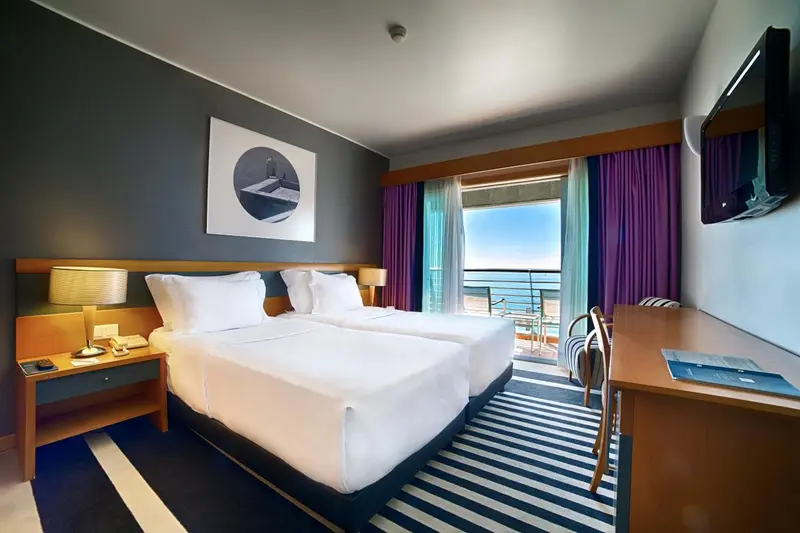 Une chambre lumineuse avec un grand lit et un balcon donnant sur la mer.