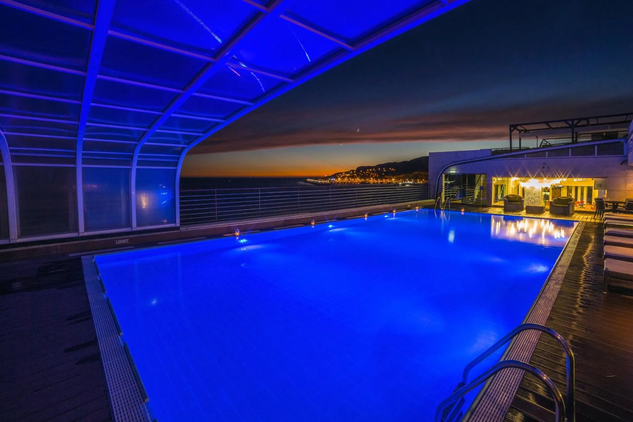 Piscine illuminée avec vue sur la mer au coucher du soleil.