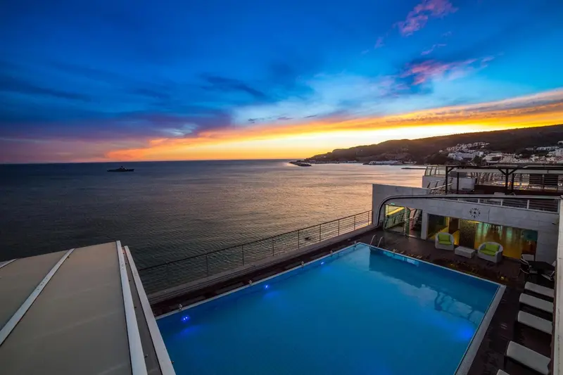 Une piscine illuminée surplombe la mer au coucher du soleil.