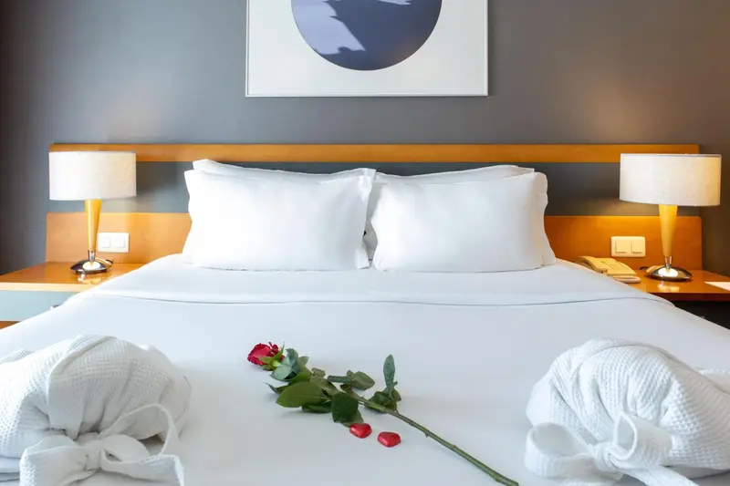 Un lit double avec des oreillers blancs et une rose rouge posée sur le drap.