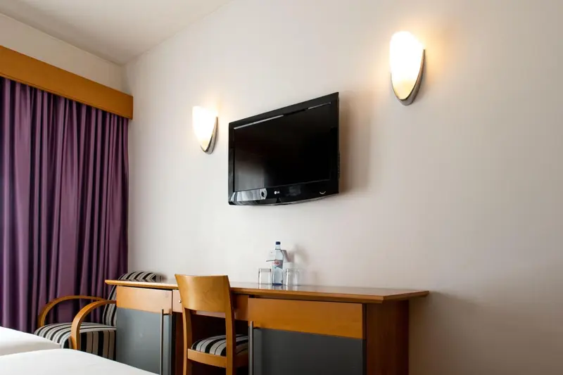 Une télévision murale domine un bureau en bois et deux chaises.