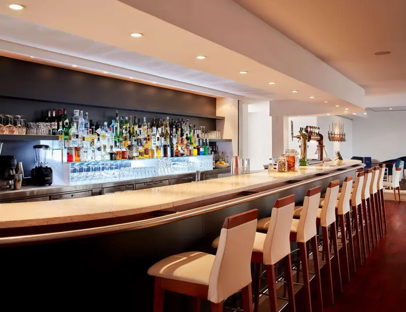 Un long comptoir de bar avec des tabourets et une sélection de boissons.