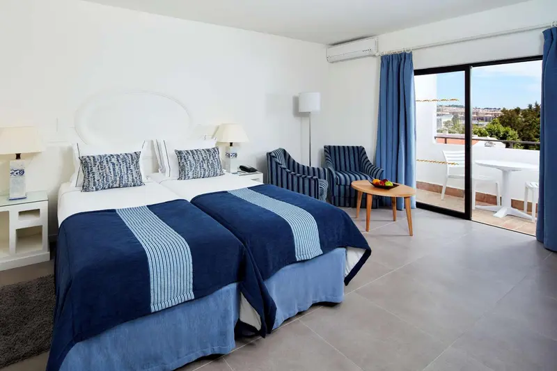 Une chambre lumineuse avec un lit double et un coin salon donnant sur une terrasse.
