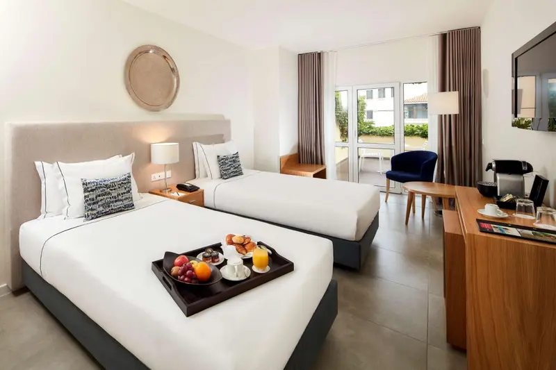 Une chambre lumineuse avec deux lits simples et un plateau de petit-déjeuner.