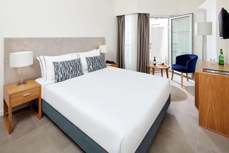 Une chambre lumineuse avec un grand lit et un fauteuil bleu.