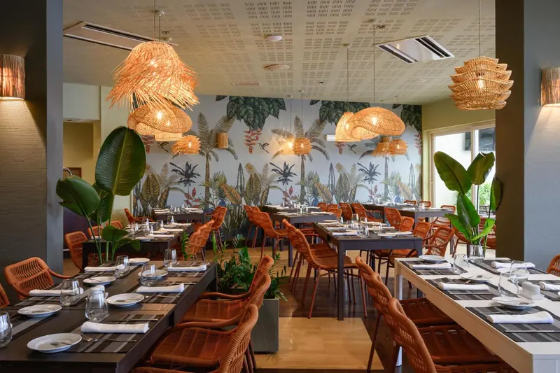 Une salle de restaurant lumineuse avec des tables dressées et une décoration tropicale.
