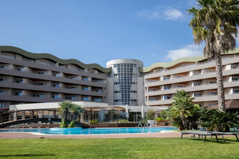 Bâtiment moderne avec des balcons surplombant une piscine et un jardin verdoyant.