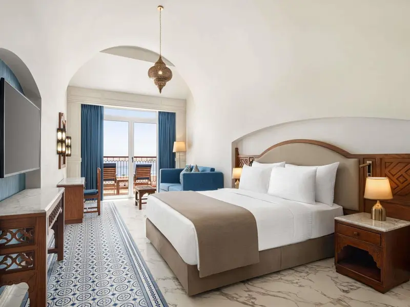 Une chambre lumineuse avec un grand lit et un coin salon près d'une fenêtre.