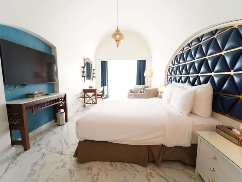 Une chambre lumineuse avec un grand lit et un espace salon attenant.