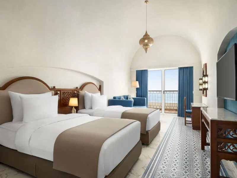 Chambre lumineuse avec deux lits simples et vue sur la mer.