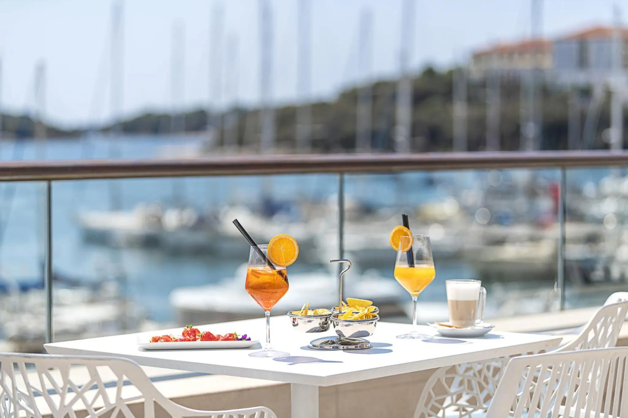 Boissons et amuse-gueules servis sur une table en terrasse avec vue sur un port de plaisance.