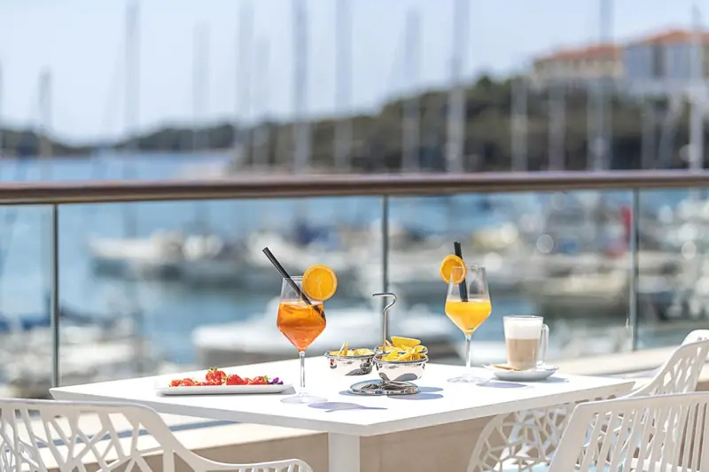Boissons et amuse-gueules servis sur une table en terrasse avec vue sur un port de plaisance.