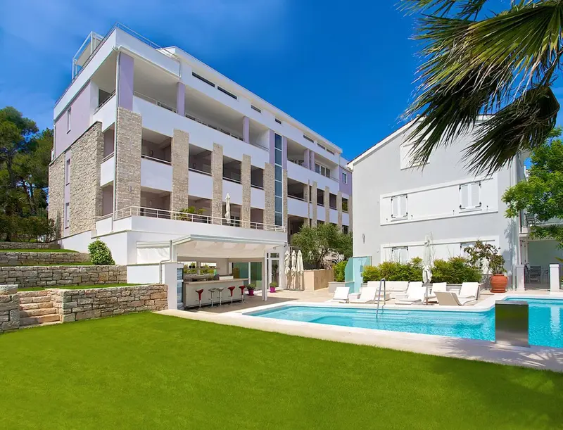 Bâtiment blanc moderne avec des balcons donnant sur une piscine et une pelouse verte.