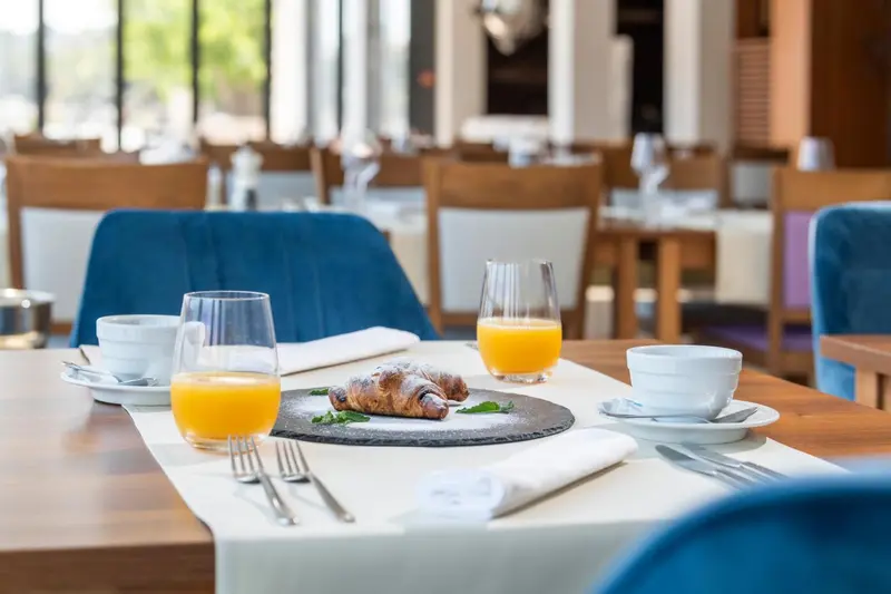 Une table est dressée avec un petit-déjeuner composé d'un croissant, d'une tasse de café et d'un jus d'orange.