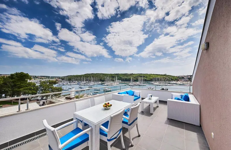 Terrasse aménagée avec mobilier blanc et vue sur un port de plaisance ensoleillé.