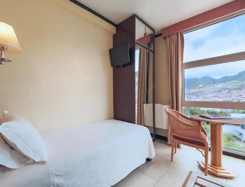 Chambre lumineuse avec un lit simple et une vue sur un paysage montagneux.